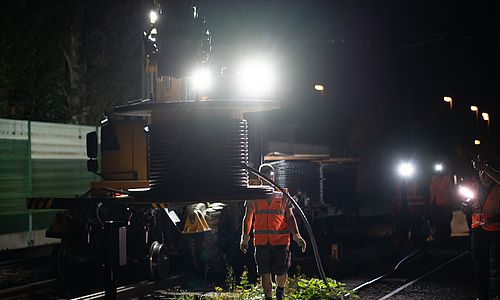 Eine nächtlichen Baustelle, die von Scheinwerfern ausgeleuchtet ist. Das Bild zeigt Arbeiten an der Leit- und Sicherungstechnik an einer Bahnstrecke.