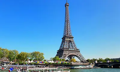 Der Eiffelturm in Paris. Im Bild-Vordergrund ist ein Ausflugsschiff zu sehen, das auf der Seine fährt.