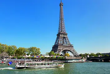 Der Eiffelturm in Paris. Im Bild-Vordergrund ist ein Ausflugsschiff zu sehen, das auf der Seine fährt.