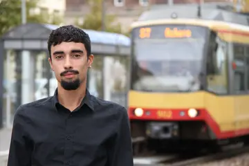 Vincent Guth steht an einem Bahnsteig. Im Hintergrund hält eine Stadtbahn der Albtal-Verkehrs-Gesellschaft.