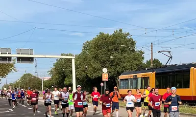 Das Foto zeigt Teilnehmer*innen des Baden-Marathons, die entlang der Durlacher Allee laufen. Im Hintergrund fährt eine Bahn vorbei.