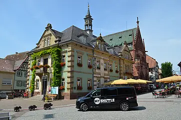 Ein schwarzes MyShuttle-Fahrzeug steht auf dem Rathausplatz in Bretten. Im Hintergrund ist das historische Rathaus zu sehen.