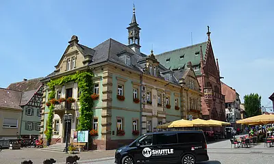 Ein schwarzes MyShuttle-Fahrzeug steht auf dem Rathausplatz in Bretten. Im Hintergrund ist das historische Rathaus zu sehen.