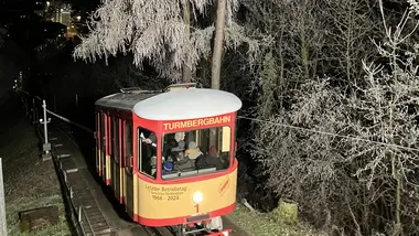 Ein historischer Wagen der Durlacher Turmbergbahn auf einer der letzten Fahrten am Abend des 29. Dezembers 2024. Neben der Bahntrasse stehen Bäume, die mit Raureif bedeckt sind.