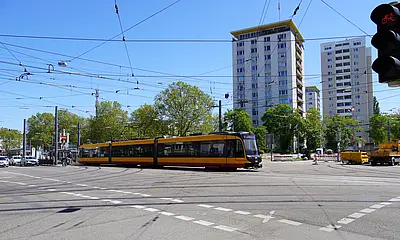Das Foto zeigt den Kreuzungsbereich am Entenfang. Eine Bahn überquert die Kreuzung. Links im Bild stehen Autos an einer Ampel. Im Bild-Hintergrund sind Hochäuser zu sehen.