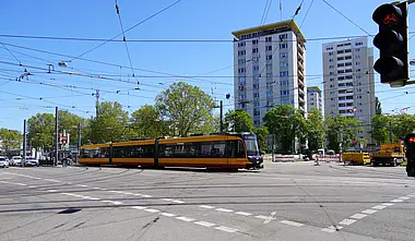Das Foto zeigt den Kreuzungsbereich am Entenfang. Eine Bahn überquert die Kreuzung. Links im Bild stehen Autos an einer Ampel. Im Bild-Hintergrund sind Hochäuser zu sehen.