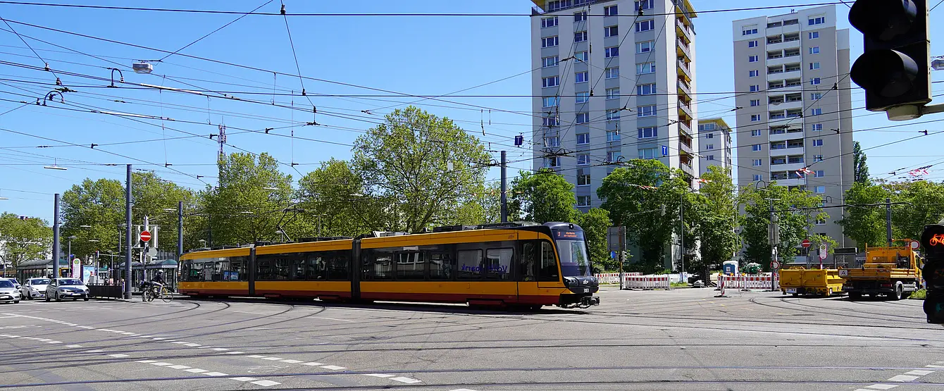 Das Foto zeigt den Kreuzungsbereich am Entenfang. Eine Bahn überquert die Kreuzung. Links im Bild stehen Autos an einer Ampel. Im Bild-Hintergrund sind Hochäuser zu sehen.