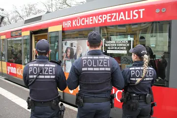 Drei Polizeibeamt*innen stehen an einer Haltestelle und beobachten eine einfahrende Straßenbahn.