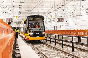 Eine schwarz-gelbe Bahn fährt durch den Stadtbahntunnel. Rechts und links der Gleise sind oragefarbene Absperrgitter aus Kunststoff aufgestellt. Ein Streckenpast mit gelber Warnweste sichert die Einfaht der Bahn.