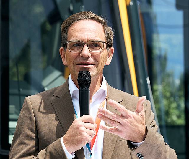 Der technische Geschäftsführer Christian Höglmeier steht vor einer Stadtbahn und spricht in ein Mikrofon.