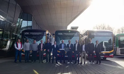 Eine Delegation der Verkehrsbetriebe Karlsruhe bekommt einen Schlüssel mit dem MAN-Logo überreicht. Im Hintergrund stehen Elektrobusse.