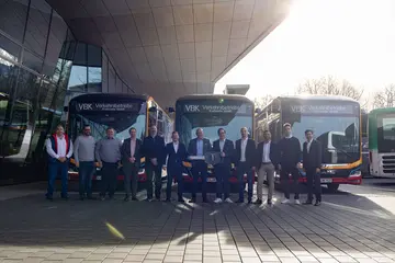 Eine Delegation der Verkehrsbetriebe Karlsruhe bekommt einen Schlüssel mit dem MAN-Logo überreicht. Im Hintergrund stehen Elektrobusse.