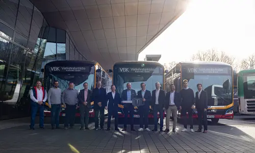 Eine Delegation der Verkehrsbetriebe Karlsruhe bekommt einen Schlüssel mit dem MAN-Logo überreicht. Im Hintergrund stehen Elektrobusse.