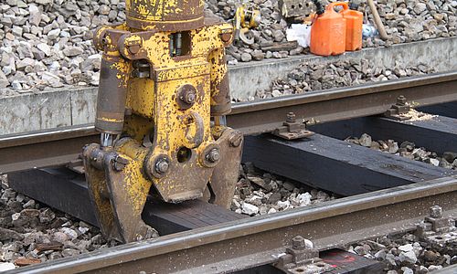 Ein gelber Greifbagger-Arm fasst eine Gleisschwelle an