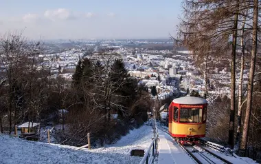 Die Turmbergbahn bei einer Fahrt im Winter. Neben der Bahntrasse liegt Schnee. Im Hintergrund sind die Dächer der Durlacher Altstadt zu sehen. 