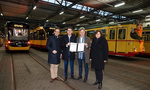 Übergabe des neuen Dienstleistungsbescheids durch Oberbürgermeister Dr. Mentrup an die VBK-Geschäftsführung im Betriebshof Gerwigstraße. Im Hintergrund stehen Straßenbahnen.