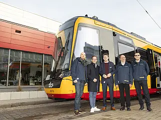 Vier Männer stehen vor dem gelb-rot lackierten VDV-TramTrain.