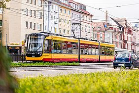 Gelb-rote Straßenbahn in der Stadt. Im Hintergrund sind Mehrfamilienhäuser zu sehen.