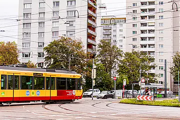 Eine Stadtbahn überquert den Kreuzungsbereich am Entenfang in Karlsruhe. Im Hintergrund sind weiße Hochhäuser und Autos zu sehen.