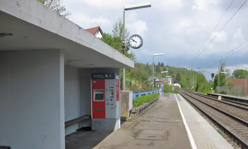 Der Bahnsteig am Haltepunkt Bilfingen: In der Wartehalle in der linken Bildhälfte ist ein Fahrkartenautomat zu sehen. Am rechten Bildrand verlaufen die Gleise der Bahnstrecke. Der Himmel ist bewölkt.