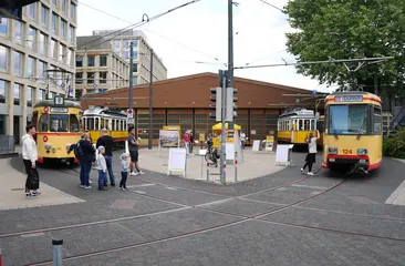 Historische Straßenbahnen stehen vor einer Wagenhalle auf dem betriebsglände der Verkehrsbetriebe Karlsruhe.. Menschen schauen sich die Fahrzeuge an.