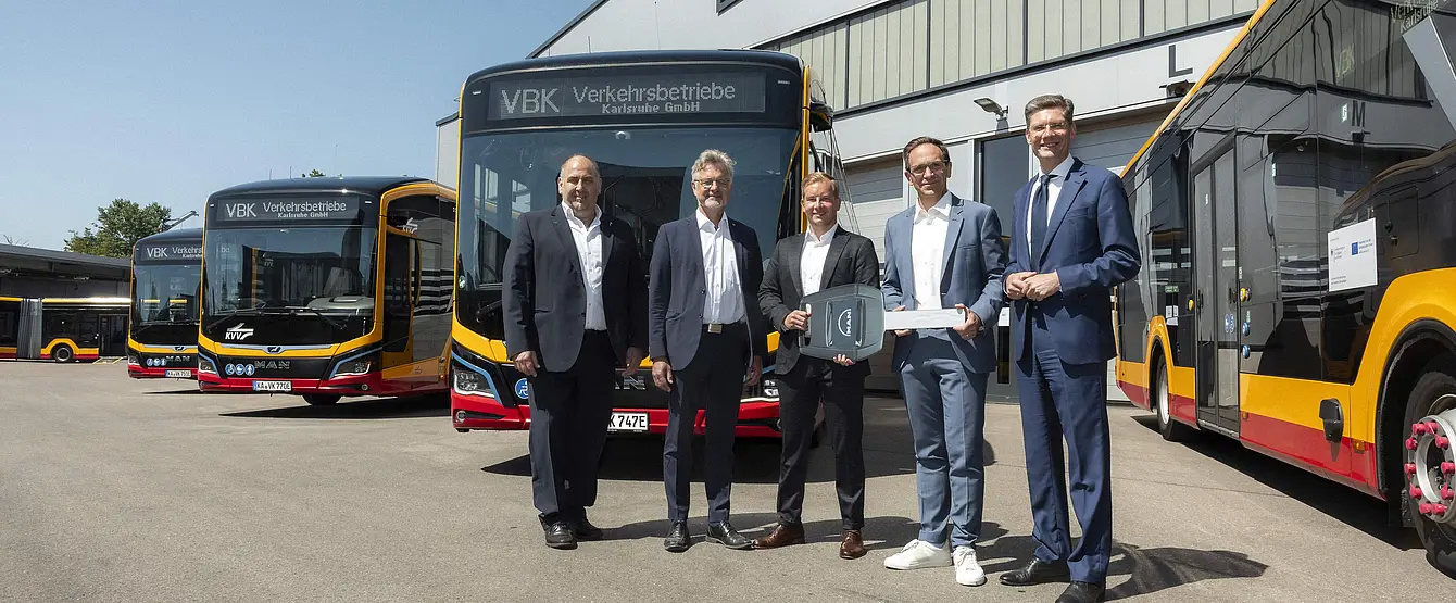 Vor E-Bussen steht eine Gruppe von Männern.