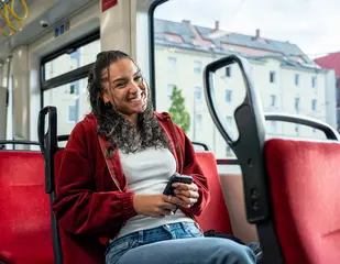 Eine junge Frau sitzt in einer Bahn und hält ein Smartphone in der Hand