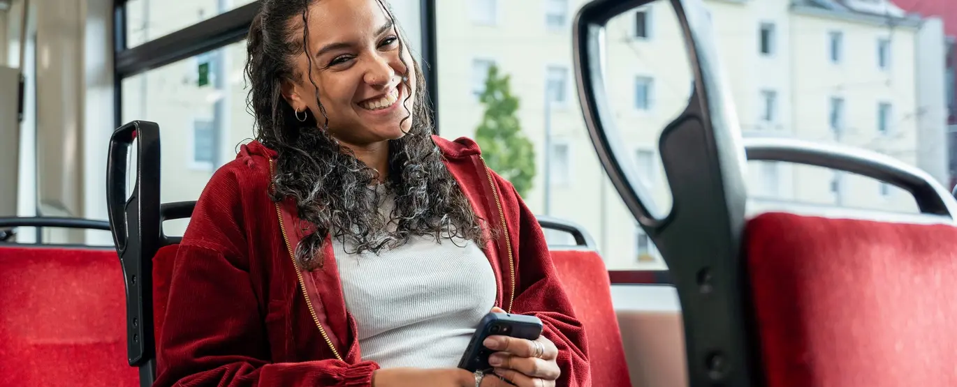 Eine junge Frau sitzt in einer Bahn und hält ein Smartphone in der Hand