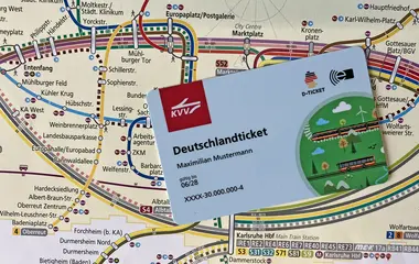 Im Bild-Vordergrund ist das Deutschlandticket zu sehen. Dahinte rliegt eine Liniennetzplan des Karslruher Verkehrsverbundes