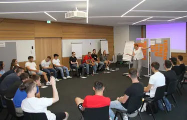 Junge Menschen sitzen in einem Stuhlkreis in einem Seminarraum und diskutieren mit einer Referentin über das Thema Nahchhaltigkeit.