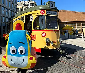 Das KVV-Maskottchen Pauly steht vor einer historischen Straßenbahn