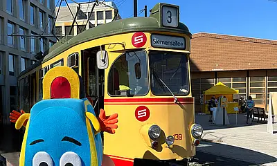 Das KVV-Maskottchen Pauly steht vor einer historischen Straßenbahn