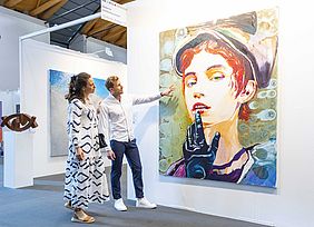 Eine Frau und ein Mann schauen ein Gemälde bei der Messe "art Karlsruhe" an.