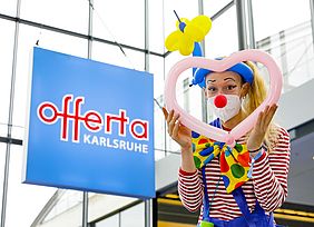 Clown mit Luftballons vor einem blauen "offerta"-Schild