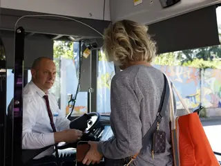 Ein Busfahrer begrüßt einen weiblichen Fahrgast beim Einstieg in das Fahrzeug.
