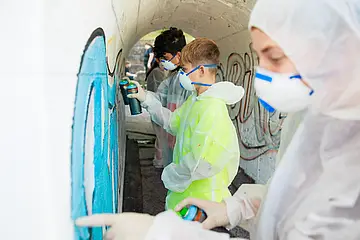 Schüler*innen gestalten mit Spraydosen die Unterführung an der Bahnhaltestelle in Baiersbronn. Dabei tragen die Schüler*innen Schutzkleidung.