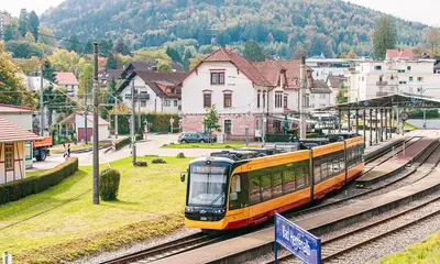Eine AVG-Stadtbahn fährt durchs Albtal. Im Hintergrund sind Häuser und der Bahnhof Bad Herrenalb zu sehenzu sehen.