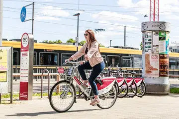 Eine Frau fährt auf einem Leih-Fahrrad von "KVV.nextbike". Im Hintergrund ist eine Straßenbahn zu sehen.