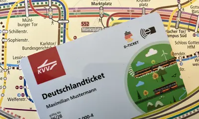 Ein Deustchlandticket im Scheckkartenformat vor einem ÖPNV-Liniennetzplan