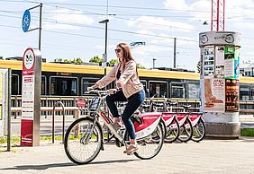 Eine frau fährt auf einem nextbike-Fahrrad. Im Hintergrund ist eine Straßenbahn zu sehen.