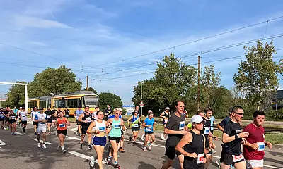 Teilnehmer*innen des Baden-Marathons in Karlsruhe laufen entlang der Durlacher Allee. Im Hintergrund fährt eine Bahn vorbei.