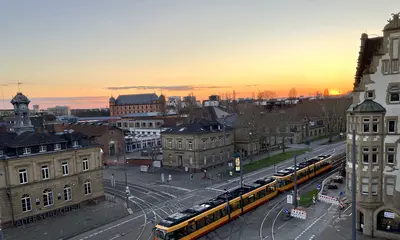 Blick von oben auf das Gleisviereck Schlachthof, Durlacher Allee und Tullastraße von schräg oben. Die untergehende Abendsonne taucht das Bild in eine dunkel-orangefarbene Lichtstimmung.