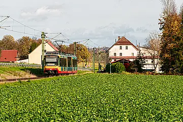 AVG-Stadtbahn fährt aus einem Wohngebiet durch die Landschaft.