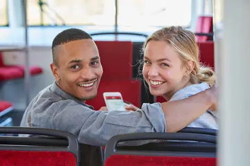 Ein junges Paar sitzt in einer Trambahn. Die Frau hält ein Smartphone in der Hand.