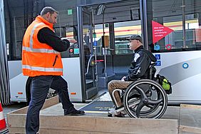 Bei einem Mobilitätstraining gibt ein Mitarbeiter der VBK einem Fahrgast in einem Rollstuhl Tipps für den sicheren Einstieg in einen Bus.