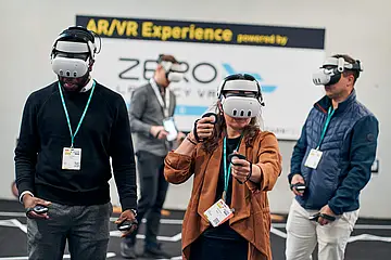 Messe-Besucher*innen bei der LEARNTEC stehen an einen Messestand und tragen VR-Brillen.