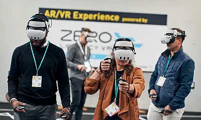 Messe-Besucher*innen bei der LEARNTEC stehen an einen Messestand und tragen VR-Brillen.