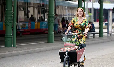 Eine Frau fährt auf einem Lastenfahrrad von KVV.nextbike. Im Hintergrund ist eine Bahn zu sehen.