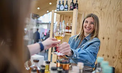An einem Messestand der "EUROVINO reicht eine Frau einem Messe-Besucher ein Weinglas. 