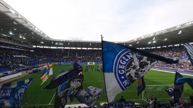 Blick aus dem KSC-Fanblock aufs Spielfeld im BBBank Wildpark . Im Fanblock werden Fahnen geschwenkt.